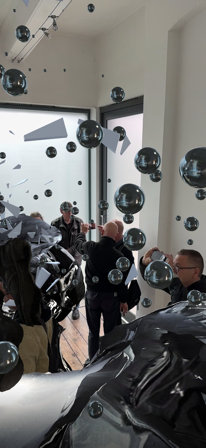 Encounter AR view in the gallery: visitors with phones among mirrored black spheres, glass shards and the crumpled wreck.