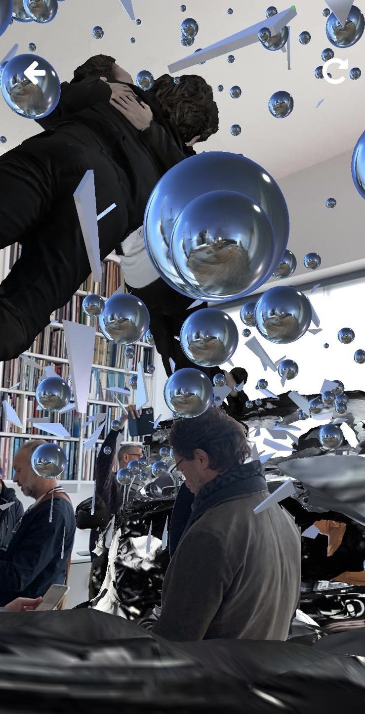 Phone AR capture of Encounter: embracing figures above a viewer and chrome spheres reflecting the room, mirrored in the spheres.