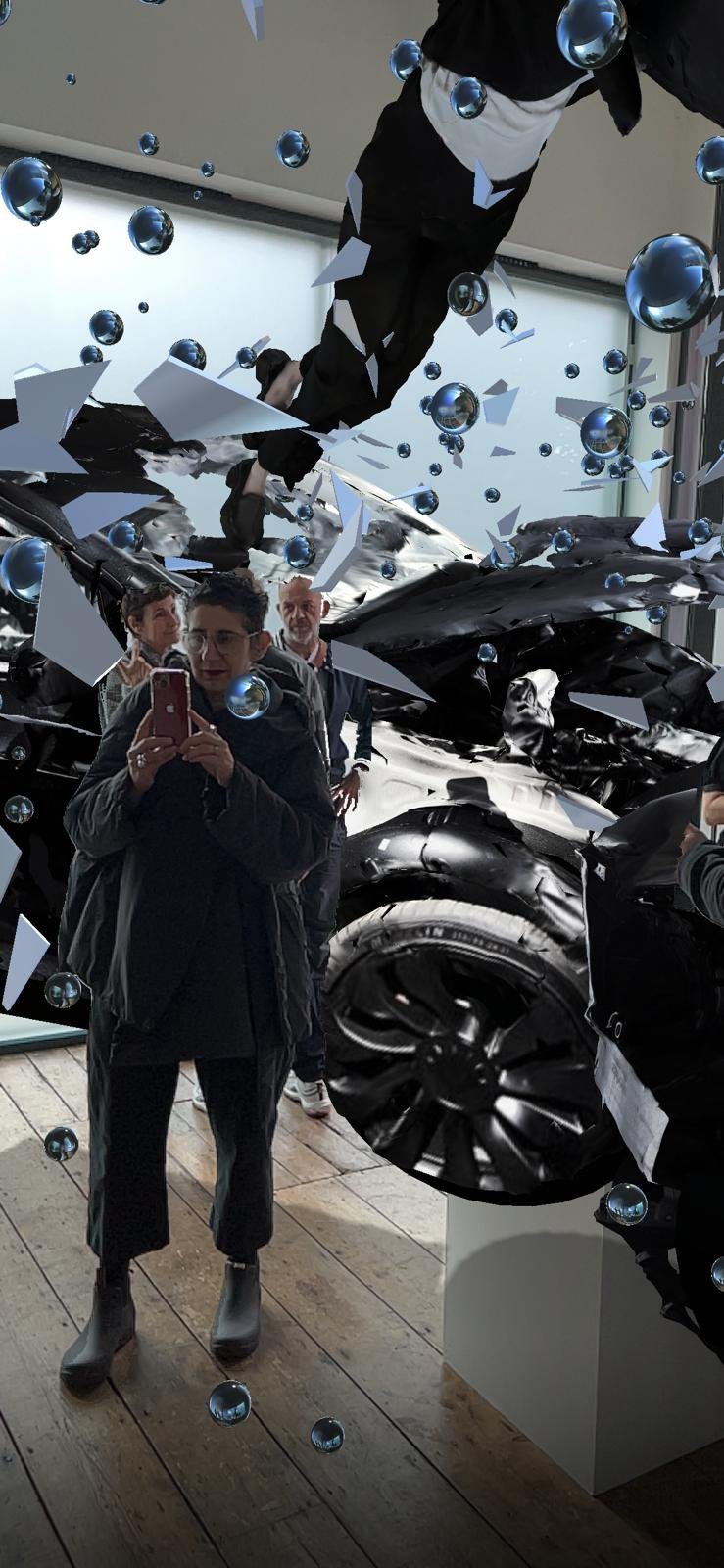 Encounter AR view in the gallery: a visitor photographs herself reflected in a shard while a black car tire and wreckage fill the foreground.