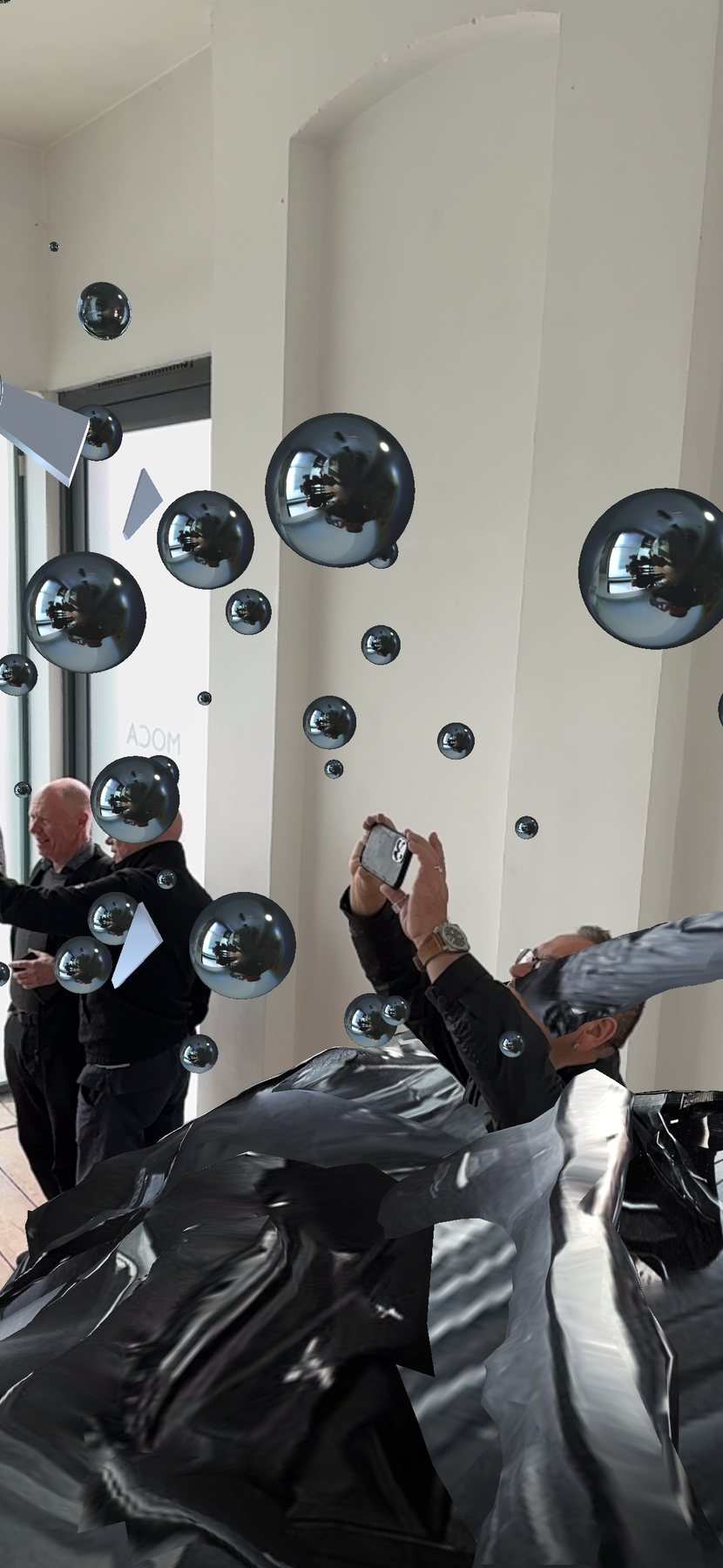 Encounter AR view: visitors with phones among chrome spheres and glass shards above the crumpled black wreck.