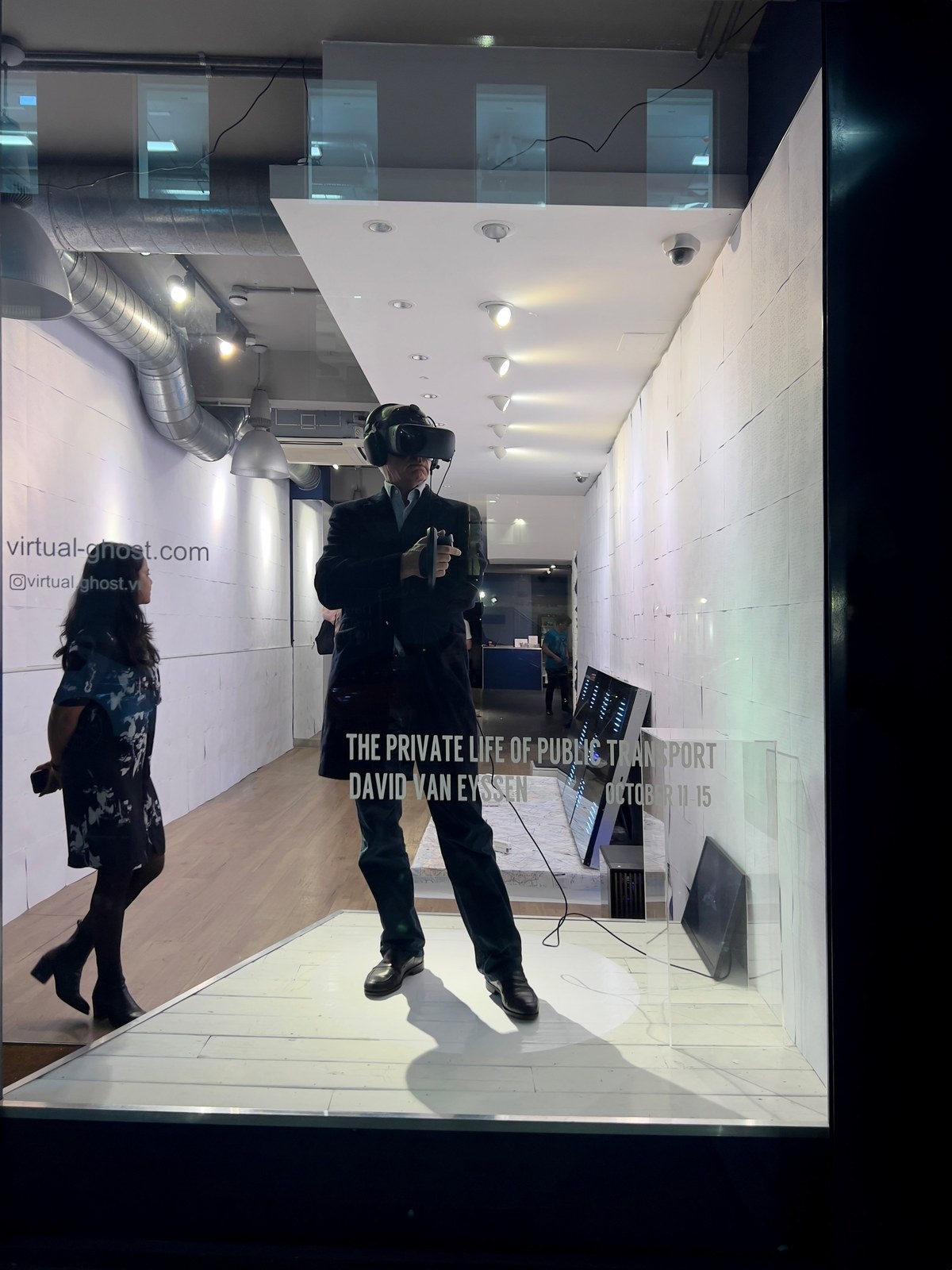 The Private Life of Public Transport: a visitor in a VR headset stands on a white platform in a London gallery window, at the Varjo Special Exhibition, as a passer-by looks on.